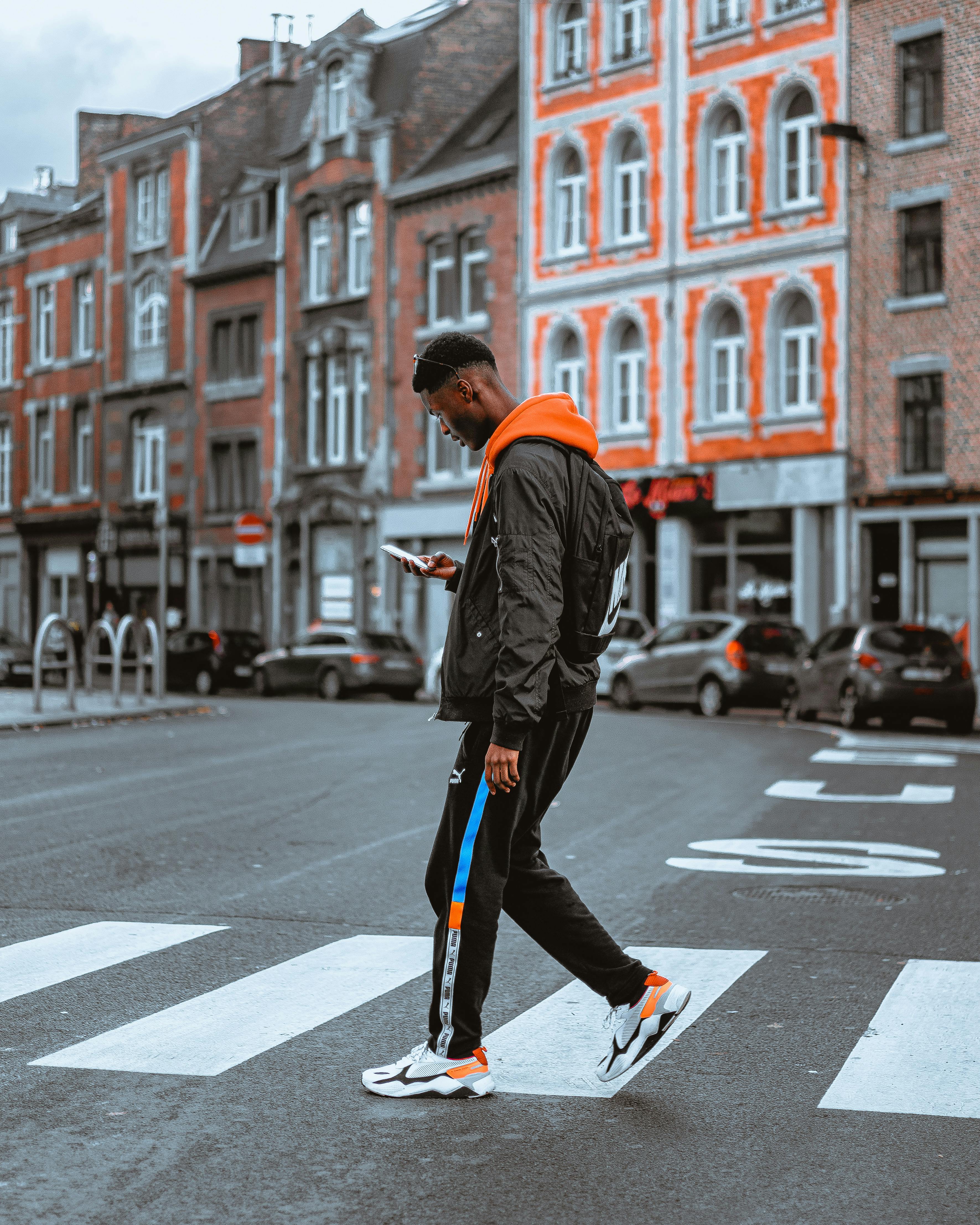 Person in orange hoodie walking on crosswalk with orange buildings
